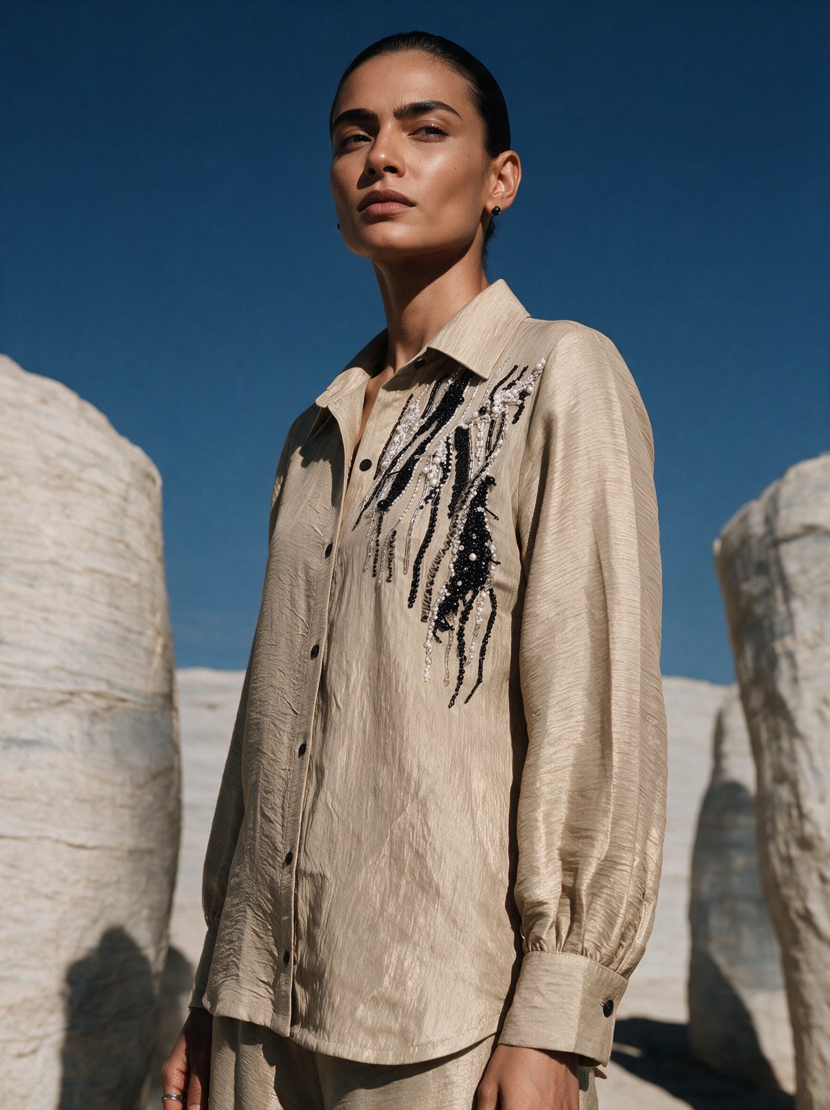 Model in a sand linen shirt with black embroidery against stone pillars and blue sky