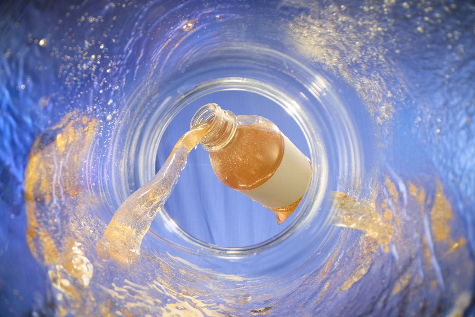 Before: studio shot of a bottle pouring amber liquid on a flat blue backdrop